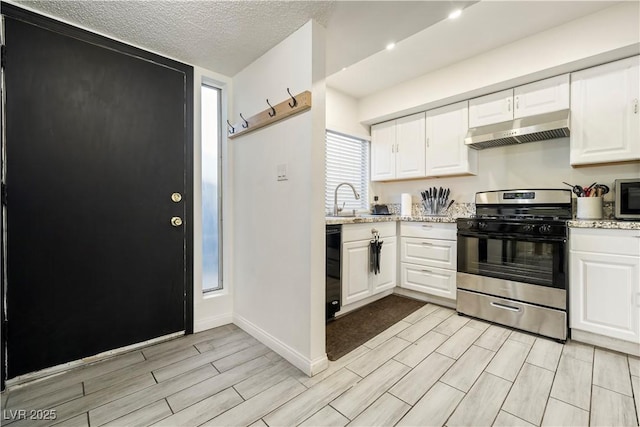 kitchen featuring stainless steel gas range oven, white cabinetry, light stone countertops, and a textured ceiling