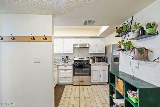 kitchen featuring white cabinetry, a textured ceiling, appliances with stainless steel finishes, and light hardwood / wood-style flooring