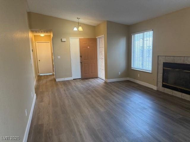 unfurnished living room featuring a tile fireplace, dark hardwood / wood-style floors, lofted ceiling, and a notable chandelier