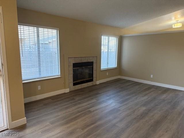 unfurnished living room featuring dark hardwood / wood-style floors, plenty of natural light, and a tiled fireplace