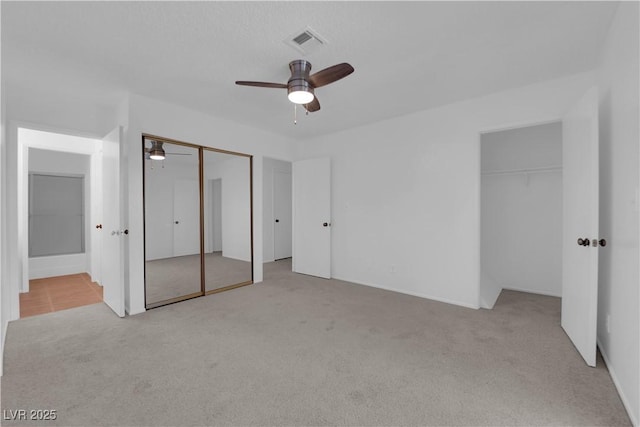 unfurnished bedroom featuring light carpet, two closets, ensuite bath, and ceiling fan