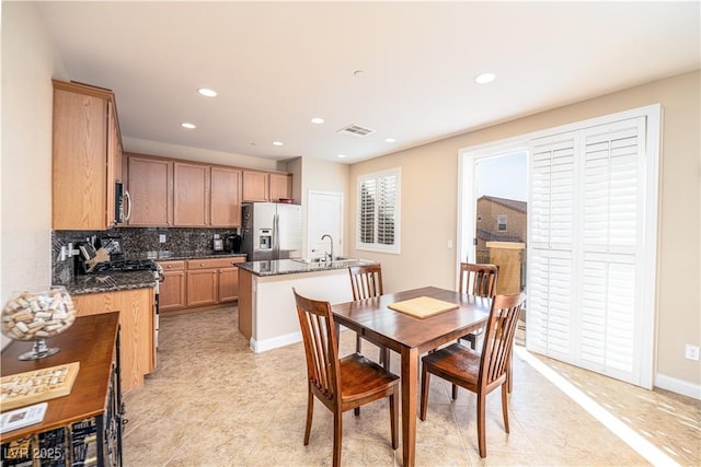 kitchen with sink, stainless steel appliances, a center island with sink, decorative backsplash, and dark stone counters