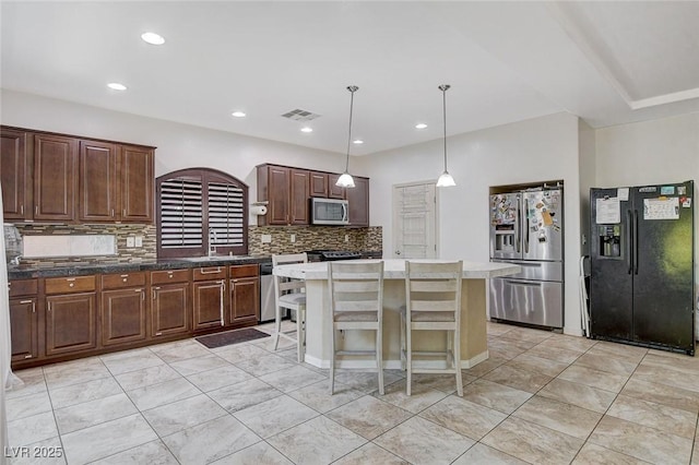 kitchen with a kitchen bar, appliances with stainless steel finishes, backsplash, decorative light fixtures, and a center island