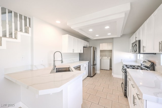 kitchen featuring kitchen peninsula, sink, appliances with stainless steel finishes, white cabinetry, and washer / clothes dryer