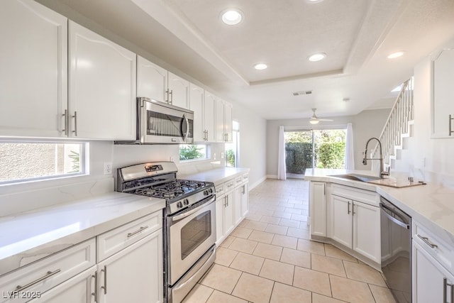 kitchen with white cabinets, appliances with stainless steel finishes, a tray ceiling, and light tile patterned flooring