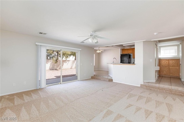 unfurnished living room with ceiling fan, light colored carpet, sink, and a wealth of natural light