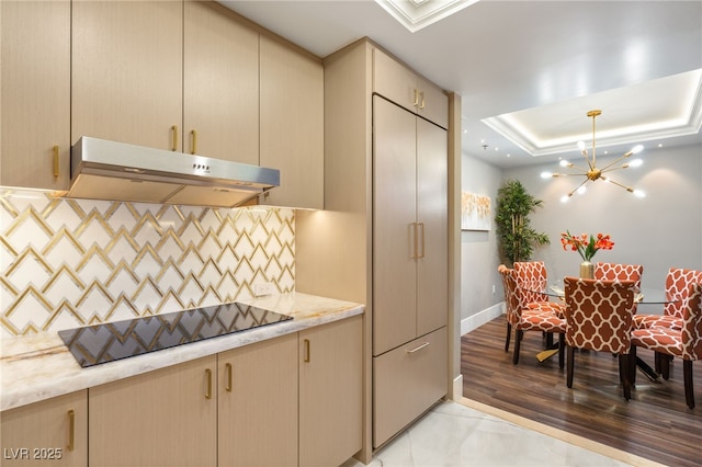 kitchen with backsplash, black electric cooktop, a raised ceiling, pendant lighting, and a chandelier