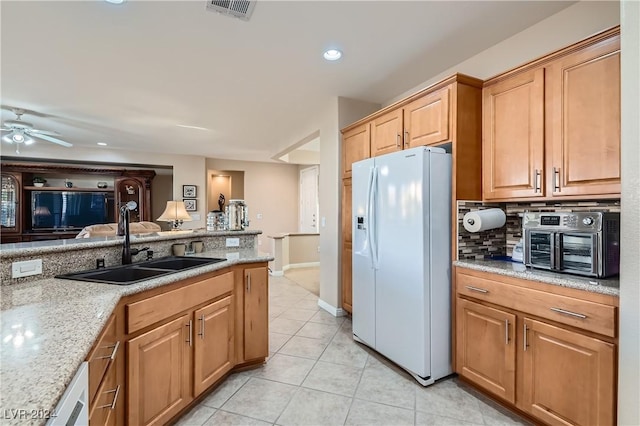 kitchen featuring white refrigerator with ice dispenser, light stone counters, light tile patterned floors, ceiling fan, and sink