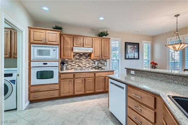 kitchen featuring light stone counters, backsplash, washer / dryer, pendant lighting, and appliances with stainless steel finishes