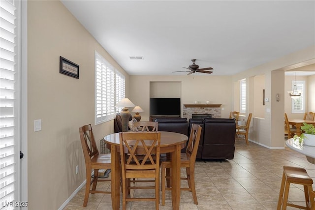 dining space featuring ceiling fan, light tile patterned floors, and a brick fireplace