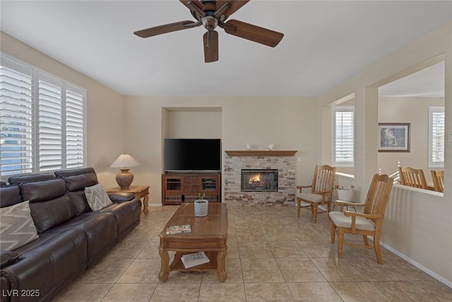 tiled living room with ceiling fan and a stone fireplace