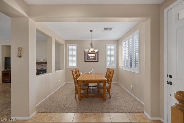 dining space featuring a notable chandelier, a stone fireplace, and light carpet