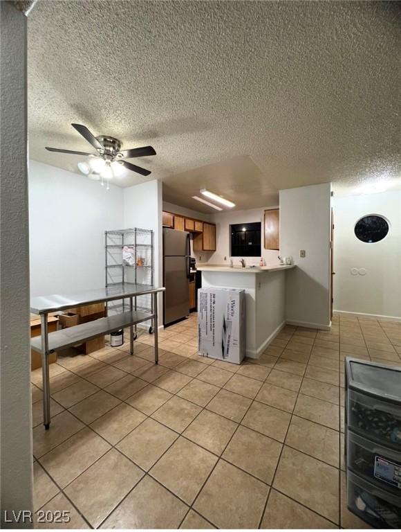 kitchen with ceiling fan, stainless steel fridge, a textured ceiling, light tile patterned flooring, and kitchen peninsula