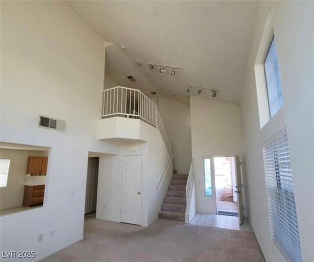 stairs with carpet flooring, a towering ceiling, and rail lighting