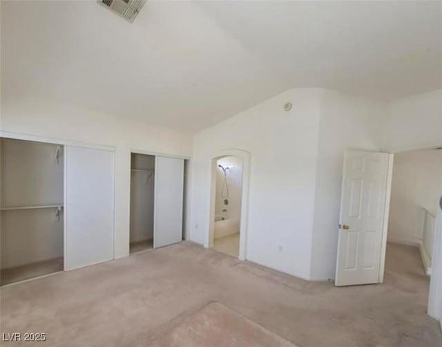 unfurnished bedroom with ensuite bathroom, vaulted ceiling, light carpet, and multiple closets