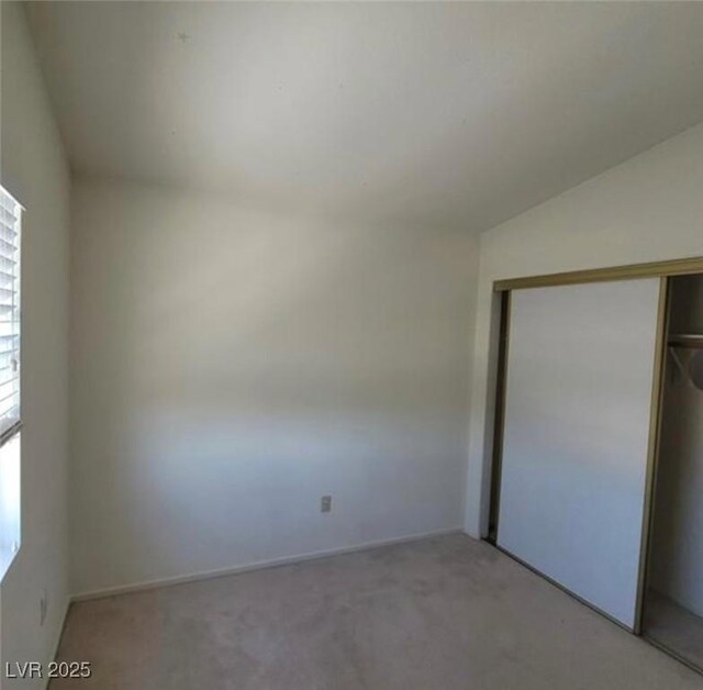 unfurnished bedroom featuring light colored carpet, a closet, and lofted ceiling