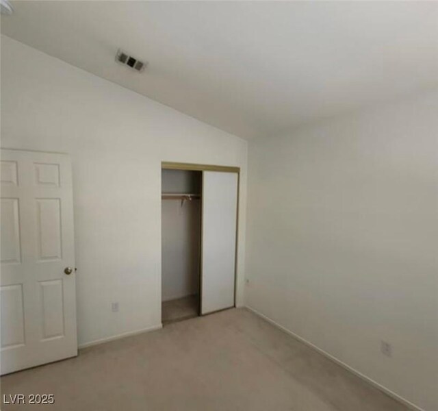 unfurnished bedroom featuring a closet, light colored carpet, and lofted ceiling