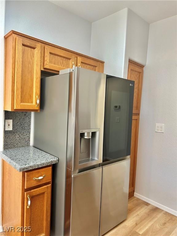 kitchen featuring stainless steel fridge with ice dispenser, light wood-type flooring, backsplash, and light stone counters