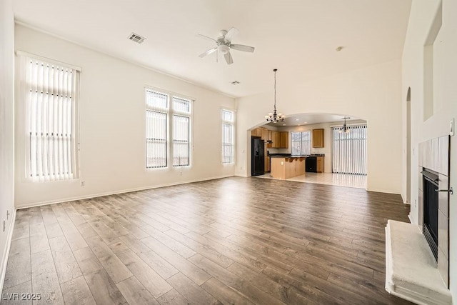 unfurnished living room with ceiling fan with notable chandelier and dark hardwood / wood-style flooring