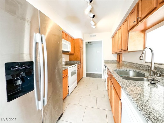 kitchen with light tile patterned flooring, sink, light stone counters, and white appliances