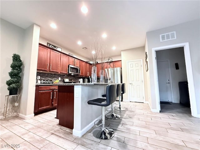 kitchen featuring backsplash, appliances with stainless steel finishes, a kitchen island with sink, and a breakfast bar area