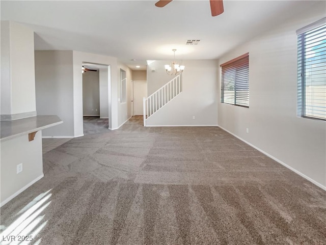 unfurnished living room featuring ceiling fan with notable chandelier and dark carpet