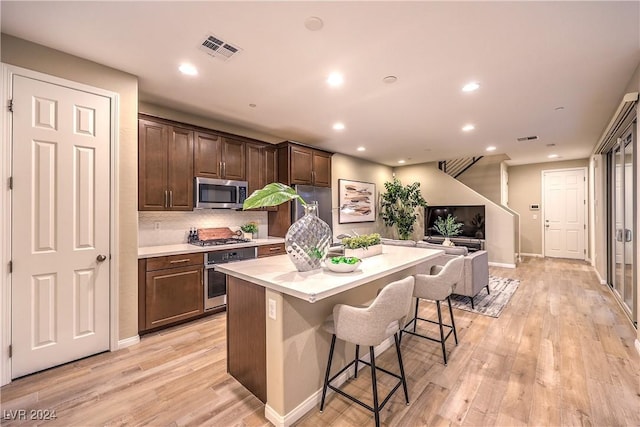 kitchen with a kitchen breakfast bar, a kitchen island, light hardwood / wood-style floors, and appliances with stainless steel finishes