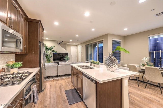 kitchen with backsplash, a kitchen island with sink, sink, light hardwood / wood-style floors, and stainless steel appliances