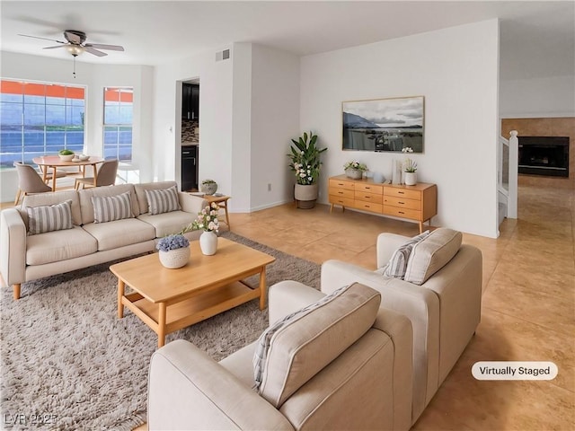 living room with a tile fireplace, ceiling fan, and light tile patterned floors