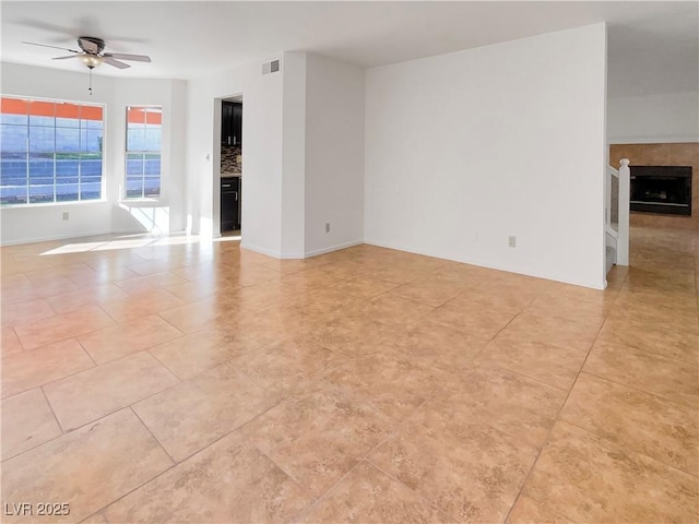 unfurnished room featuring ceiling fan, a fireplace, and light tile patterned floors