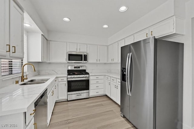 kitchen with white cabinets, sink, light stone countertops, light hardwood / wood-style floors, and stainless steel appliances