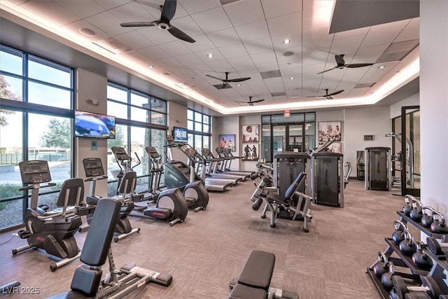 gym featuring light carpet, a towering ceiling, ceiling fan, and a paneled ceiling