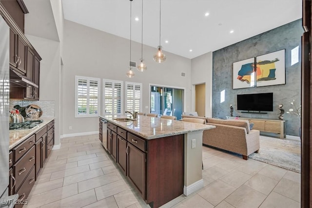 kitchen featuring pendant lighting, stainless steel gas stovetop, a kitchen island with sink, sink, and light stone counters