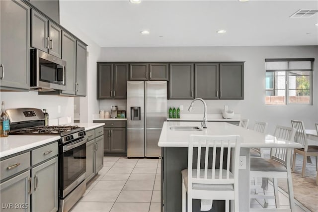 kitchen featuring a breakfast bar, sink, light tile patterned floors, an island with sink, and appliances with stainless steel finishes