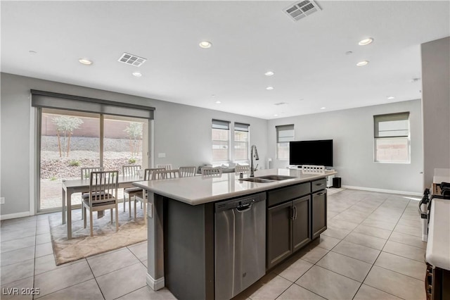 kitchen with dark brown cabinetry, sink, stainless steel dishwasher, a kitchen island with sink, and light tile patterned floors