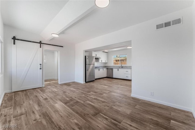 unfurnished living room featuring beamed ceiling, a barn door, light hardwood / wood-style flooring, and sink