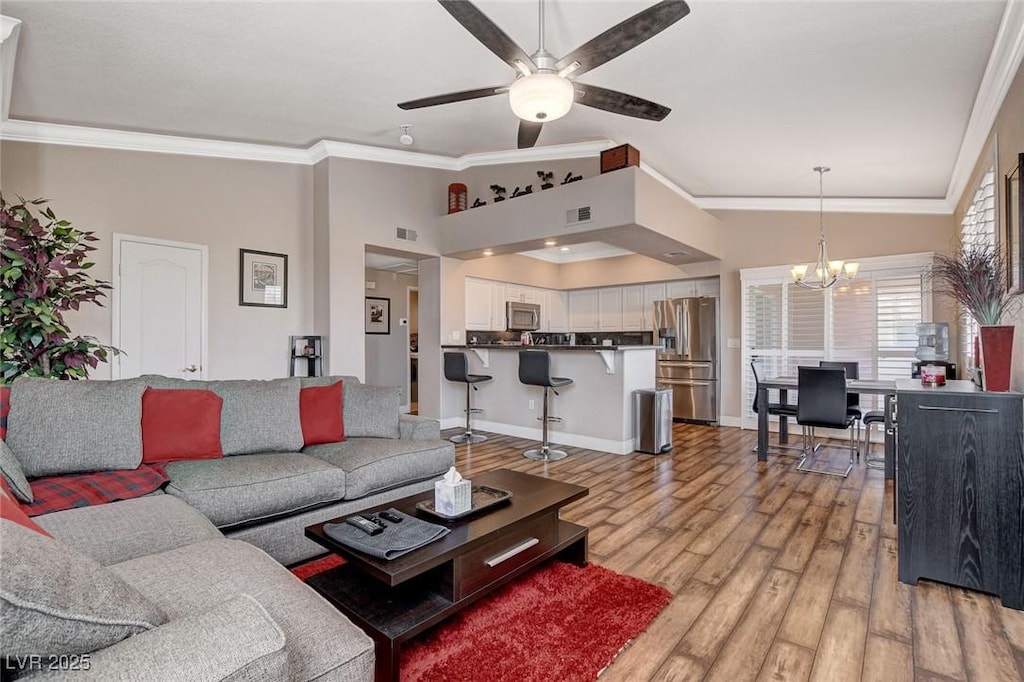 living room with ceiling fan with notable chandelier, light wood-type flooring, ornamental molding, and vaulted ceiling