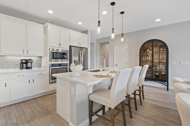 kitchen with a kitchen island with sink, sink, stainless steel appliances, and decorative light fixtures