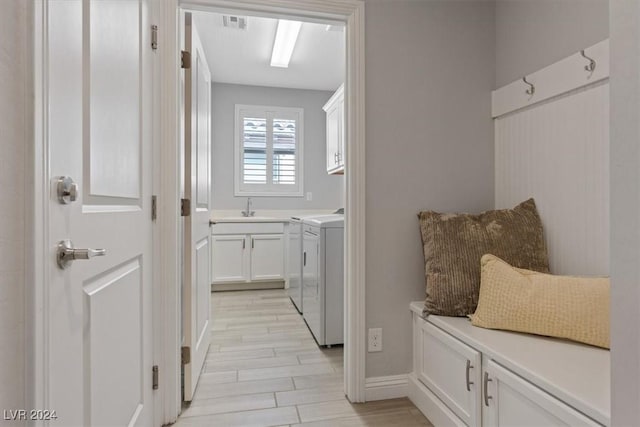 laundry room with washer and clothes dryer, cabinets, light wood-type flooring, and sink