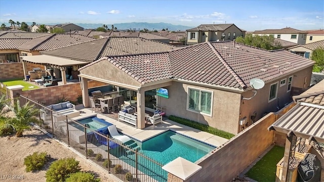 rear view of house with exterior kitchen, an outdoor living space, a mountain view, a fenced in pool, and a patio area