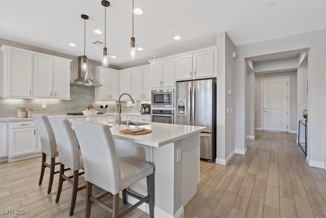 kitchen with appliances with stainless steel finishes, white cabinetry, wall chimney exhaust hood, and sink