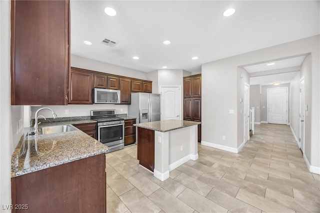 kitchen with light stone countertops, appliances with stainless steel finishes, sink, a kitchen island, and light tile patterned flooring