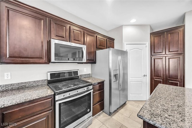 kitchen featuring dark brown cabinetry, stainless steel appliances, light stone counters, and light tile patterned flooring