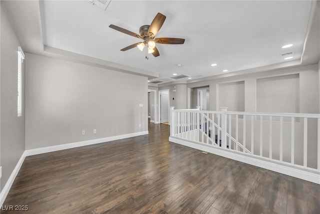 empty room featuring ceiling fan, dark wood-type flooring, and a tray ceiling