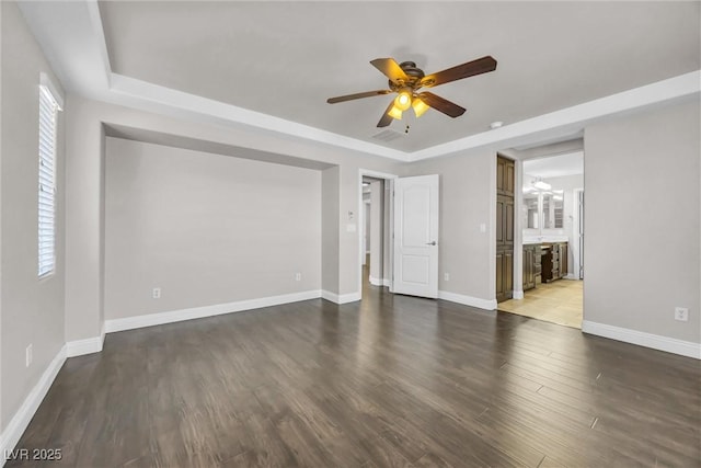 empty room featuring a raised ceiling, ceiling fan, and dark hardwood / wood-style flooring