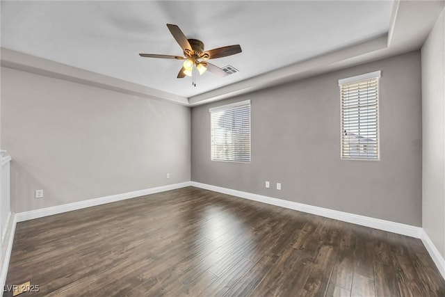 unfurnished room featuring a raised ceiling, ceiling fan, and dark hardwood / wood-style floors