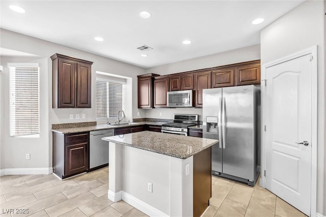 kitchen with a center island, sink, light stone countertops, dark brown cabinetry, and stainless steel appliances