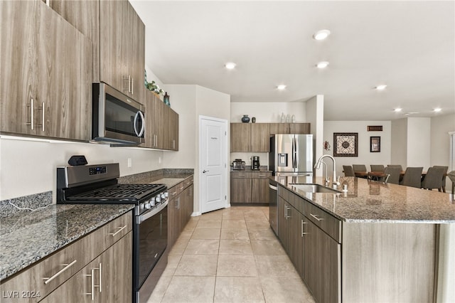 kitchen featuring stainless steel appliances, a kitchen island with sink, dark stone counters, and sink