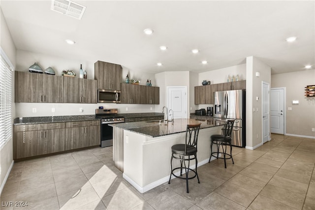 kitchen with sink, dark stone countertops, a kitchen bar, a center island with sink, and appliances with stainless steel finishes