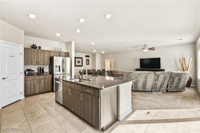 kitchen featuring dark stone counters, ceiling fan, sink, dishwasher, and an island with sink